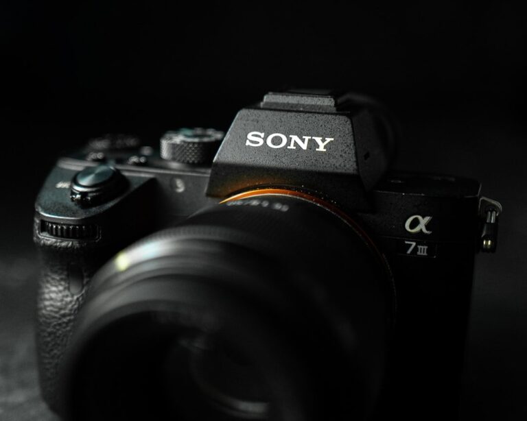 A profile shot of the white Sony FE 100-400mm f/4.5-5.6 GM OSS telephoto lens with its lens hood attached, shown against a clean background.